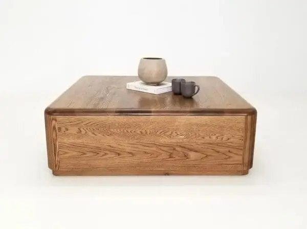 A square coffee table with a vase on top of it and mugs.