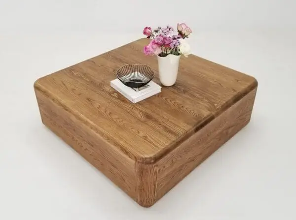 A square coffee table with a vase on top of it.