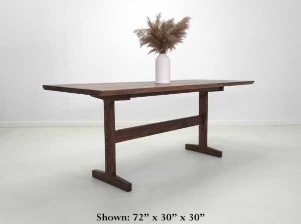 A walnut oak trestle table with a vase on top.