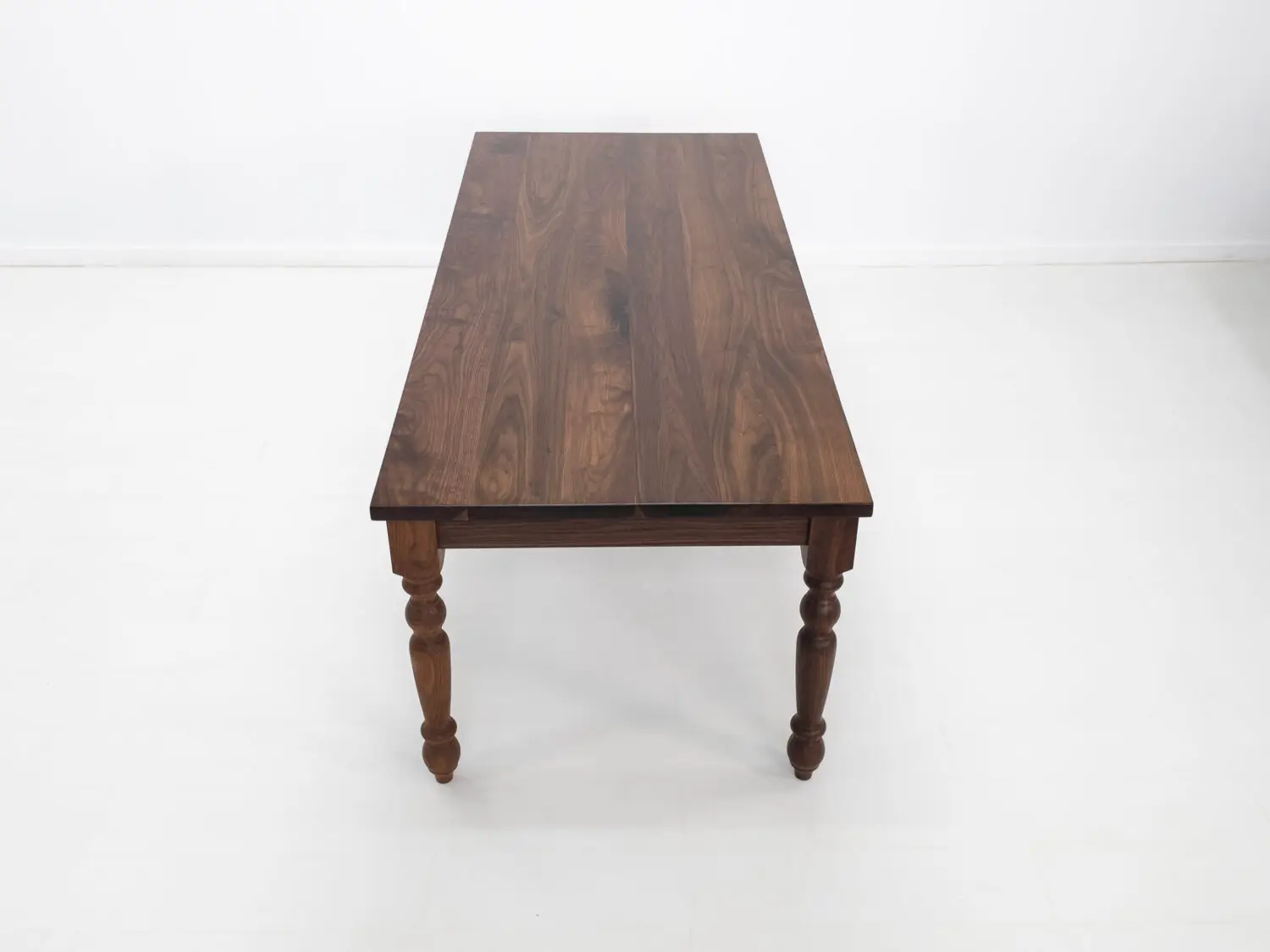 Close up of the TESS tables 1⅜ inch thick plank top highlighting the natural walnut grain and smooth hardwax oil finish
