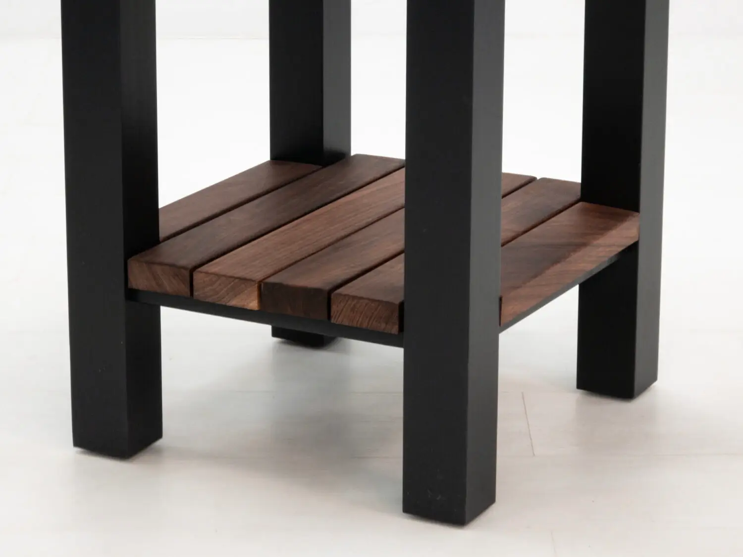Detail of lower slatted walnut shelf between black painted legs