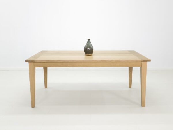 A white oak dining table with tapered legs and a vase on top.
