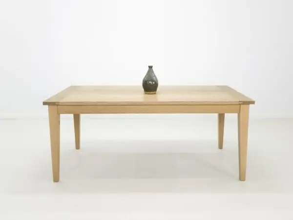 A white oak dining table with tapered legs and a vase on top.