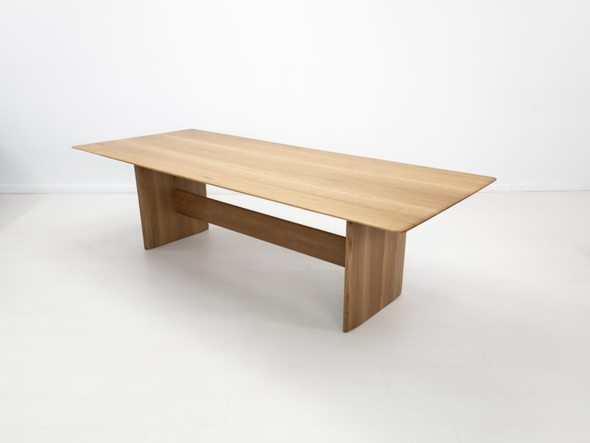 Side view of the THEO dining table with a trestle base and softly rounded corners