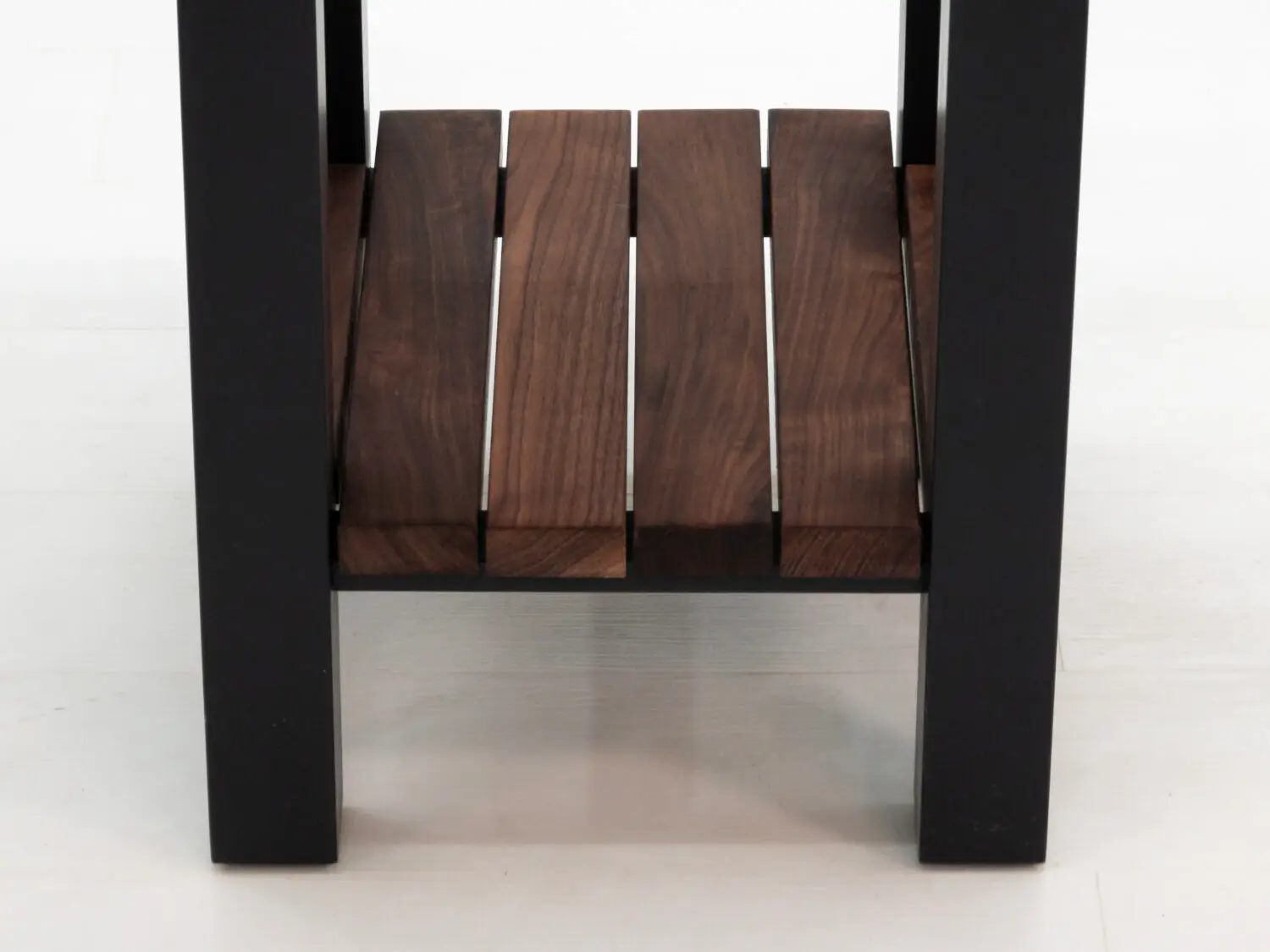 Detail of lower slatted walnut shelf between black painted legs