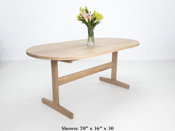 A oval top trestle dining table with two legs and flowers on top of it.