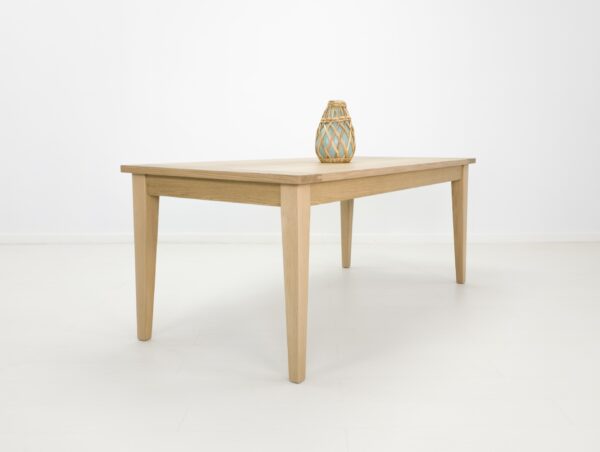 A white oak dining table with tapered legs and a vase on top.