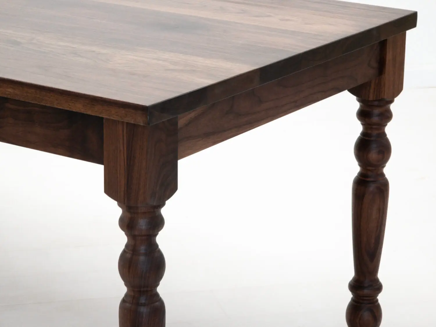 Close up of the TESS tables 1⅜ inch thick plank top highlighting the natural walnut grain and smooth hardwax oil finish