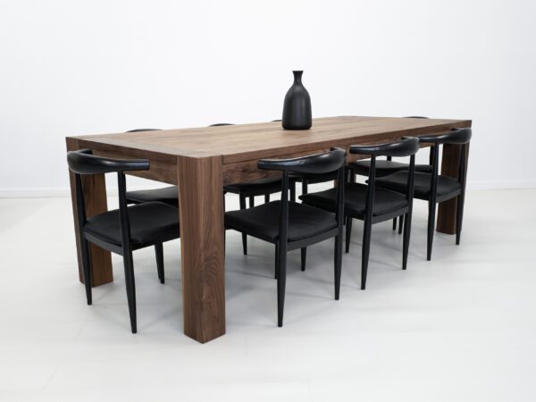 A solid walnut dining table with massive square legs and chairs around it.