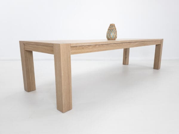 A white oak, square leg dining table with a cerused finish and decor on top.
