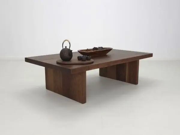 A dark wooden coffee table with a teapot and a bowl of nuts on top of it.