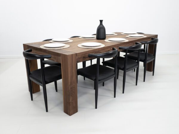 A solid walnut dining table with square legs and chairs around it.