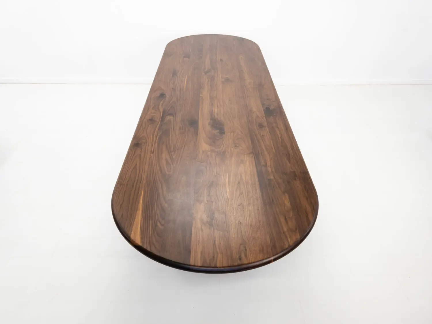 Front view of the HANA dining table in solid walnut  Showcasing its capsule oval top with a rounded bullnose edge and full base with two stretchers