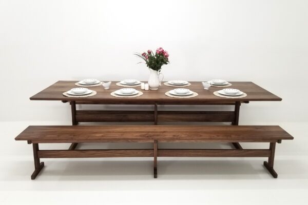 A BRIT Trestle dining table with a beveled edge, two benches, and a vase of flowers.
