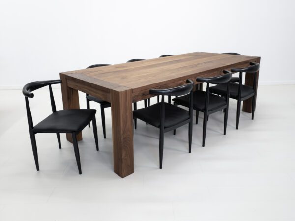 A solid walnut dining table with square legs and chairs around it.
