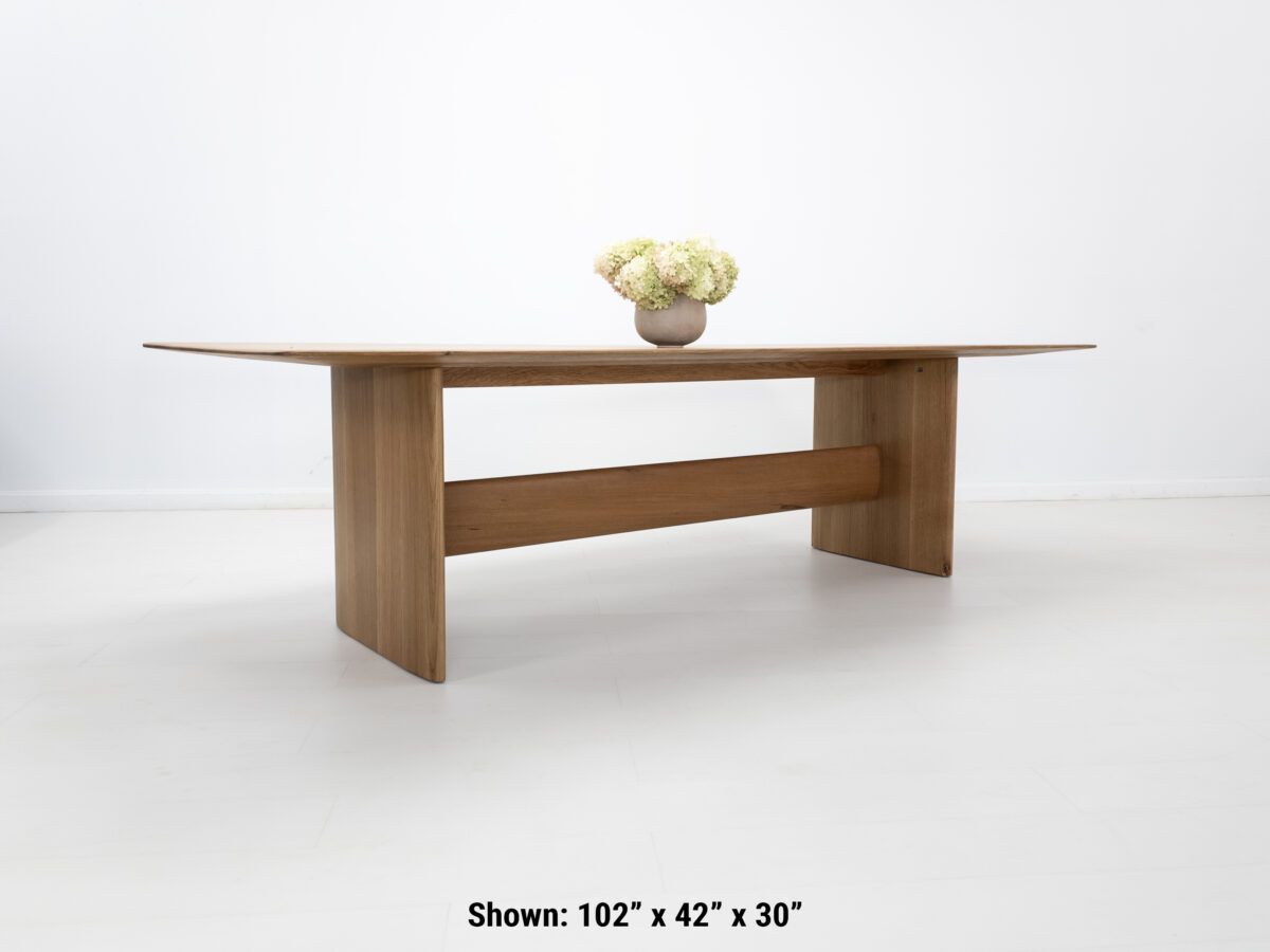 Side view of the THEO dining table with a trestle base and softly rounded corners