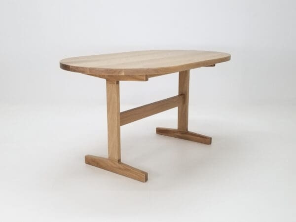 A oval top trestle dining table with two legs and decor on top of it.