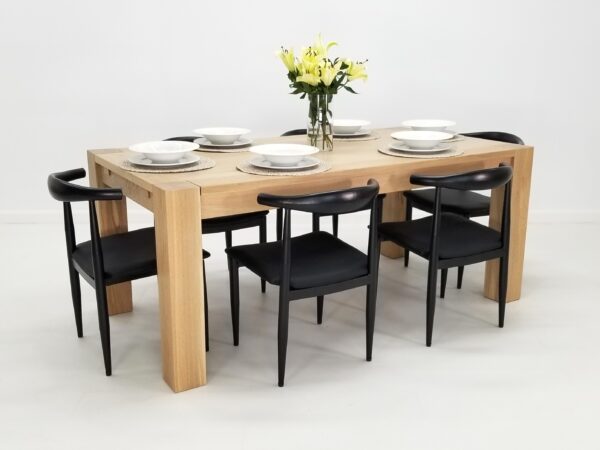 An JAQI Colossal Leg Parsons dining table with four black chairs.
