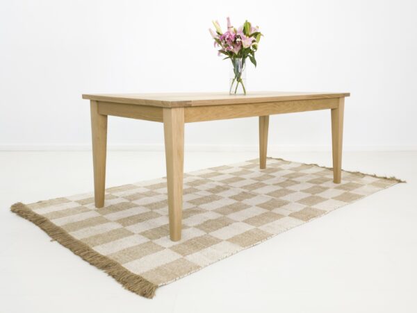 A white oak dining table on a rug with flowers on top of it.