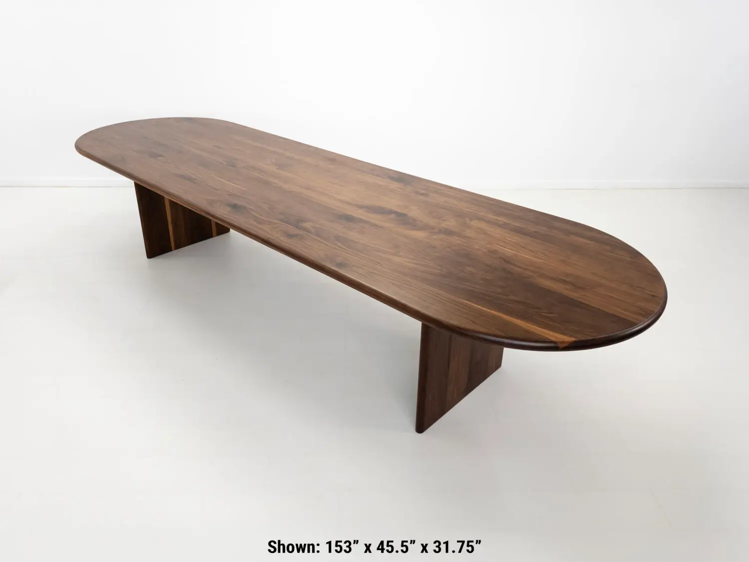 Front view of the HANA dining table in solid walnut  Showcasing its capsule oval top with a rounded bullnose edge and full base with two stretchers