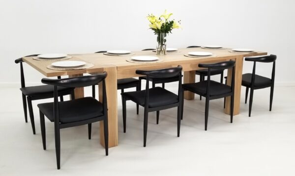 A JAQI Colossal Leg Parsons Dining Table with six black chairs and a vase.