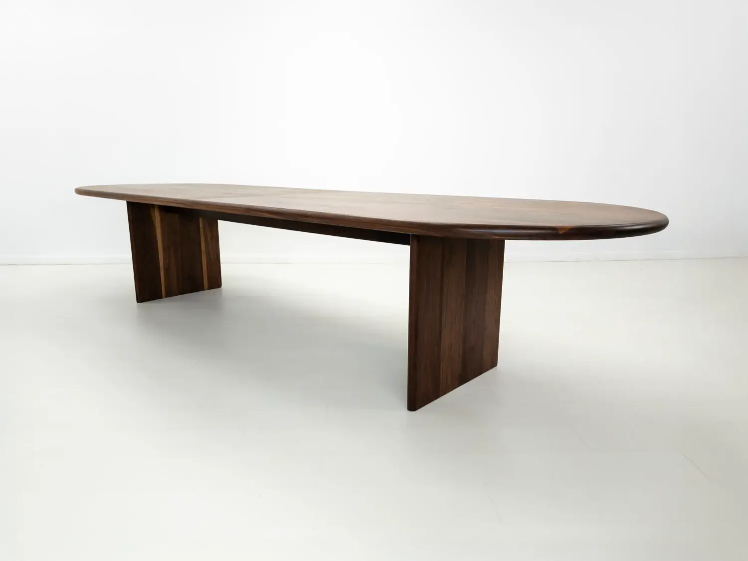 Front view of the HANA dining table in solid walnut  Showcasing its capsule oval top with a rounded bullnose edge and full base with two stretchers