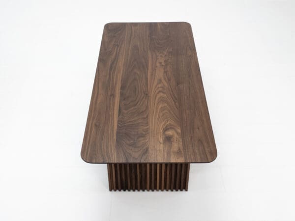 A close up on the top of a walnut coffee table with ribbed legs.