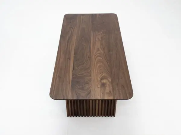 A close up on the top of a walnut coffee table with ribbed legs.