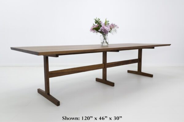 A walnut oak trestle table with a vase on top.