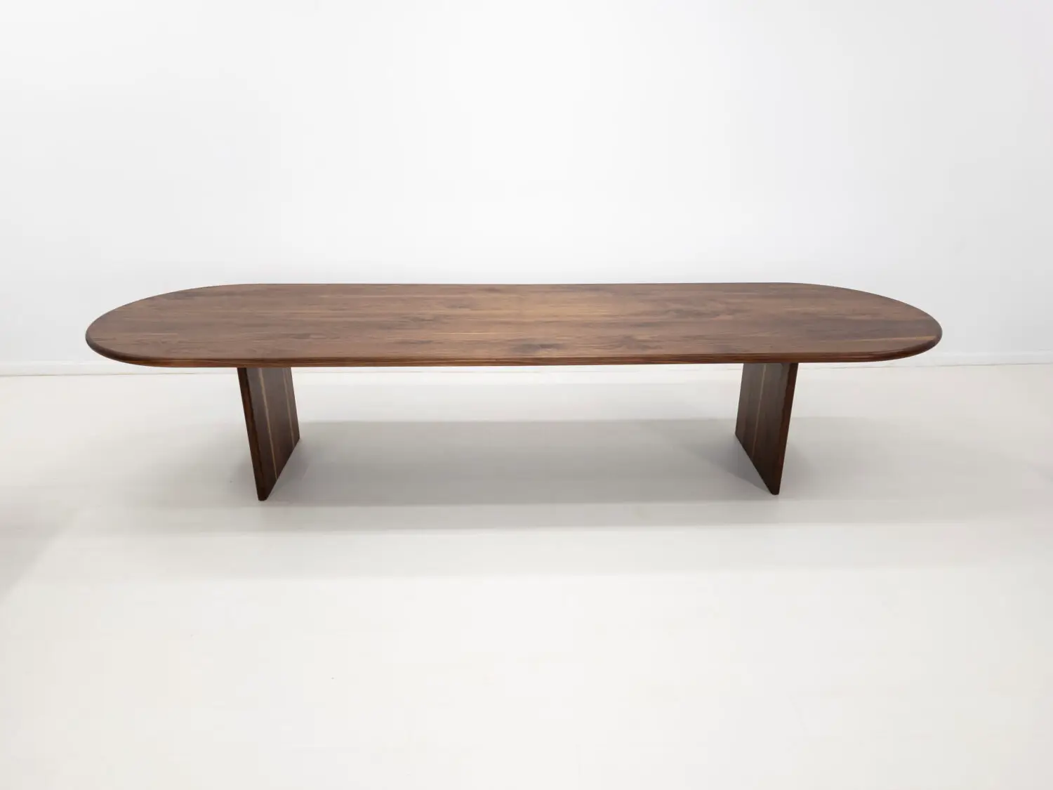 Front view of the HANA dining table in solid walnut  Showcasing its capsule oval top with a rounded bullnose edge and full base with two stretchers