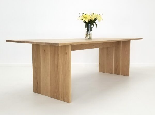A white oak panel dining table with flowers on top of it.