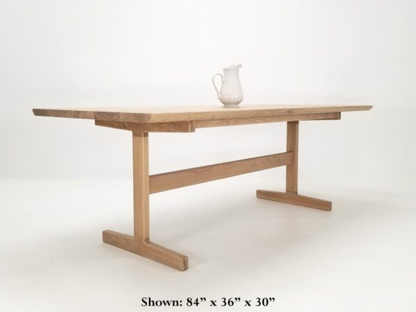 A white oak trestle table with a vase on top.