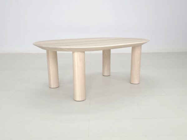 A small oval COVE coffee table with wooden legs in a white room.