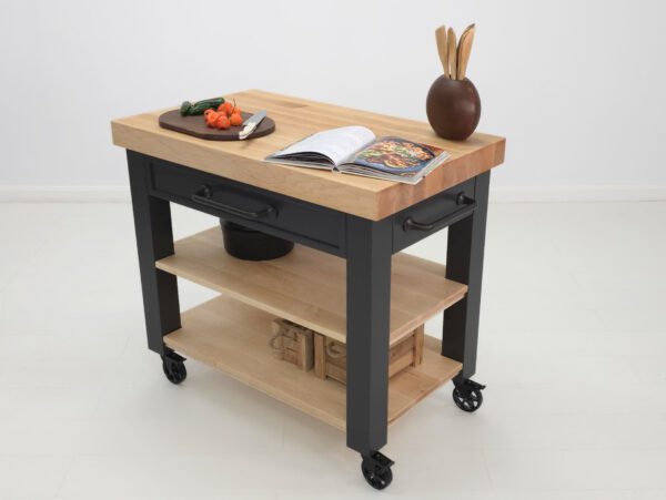 An image of a butcher block kitchen cart with a cook book and vegetables on top.
