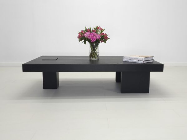 A unique black coffee table with flowers and books on top of it.