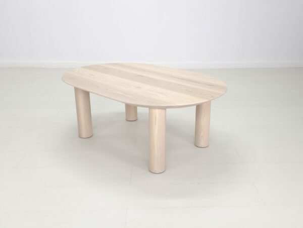 A small oval custom COVE Coffee Table with wooden legs in a white room.