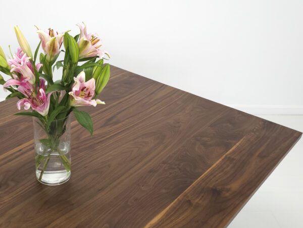 A close up of a walnut trestle dining table with flowers on top of it.