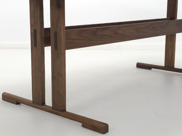 A close up of the legs and feet of a walnut trestle table.