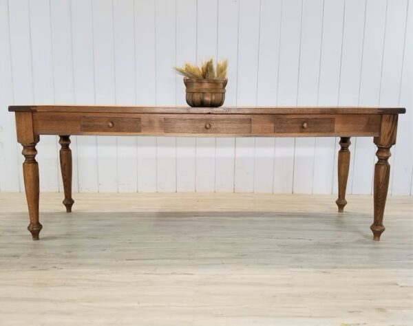 A antique style farmhouse table with drawers and a basket on top.