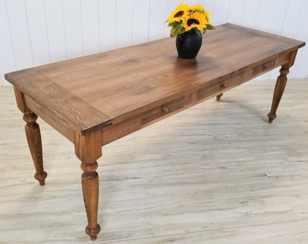 A farmhouse table with drawers and flowers on top of it.
