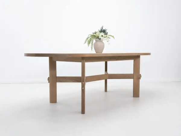 A white oak dining table with an angular stretcher design and decor on top of it.