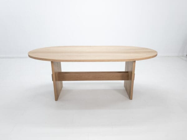 A double stretcher white oak trestle table with an oval top.