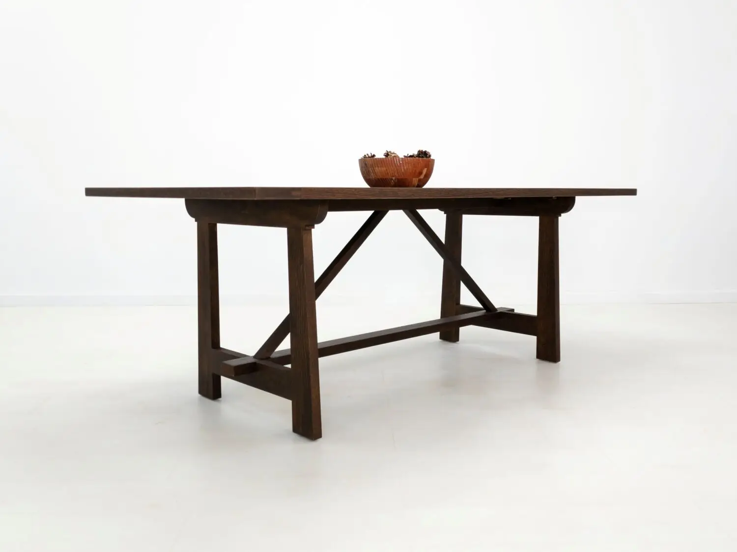 Angled view of the EDEN dining table  Custom white oak dining table in a rich stain featuring a seamless top and structural trestle base