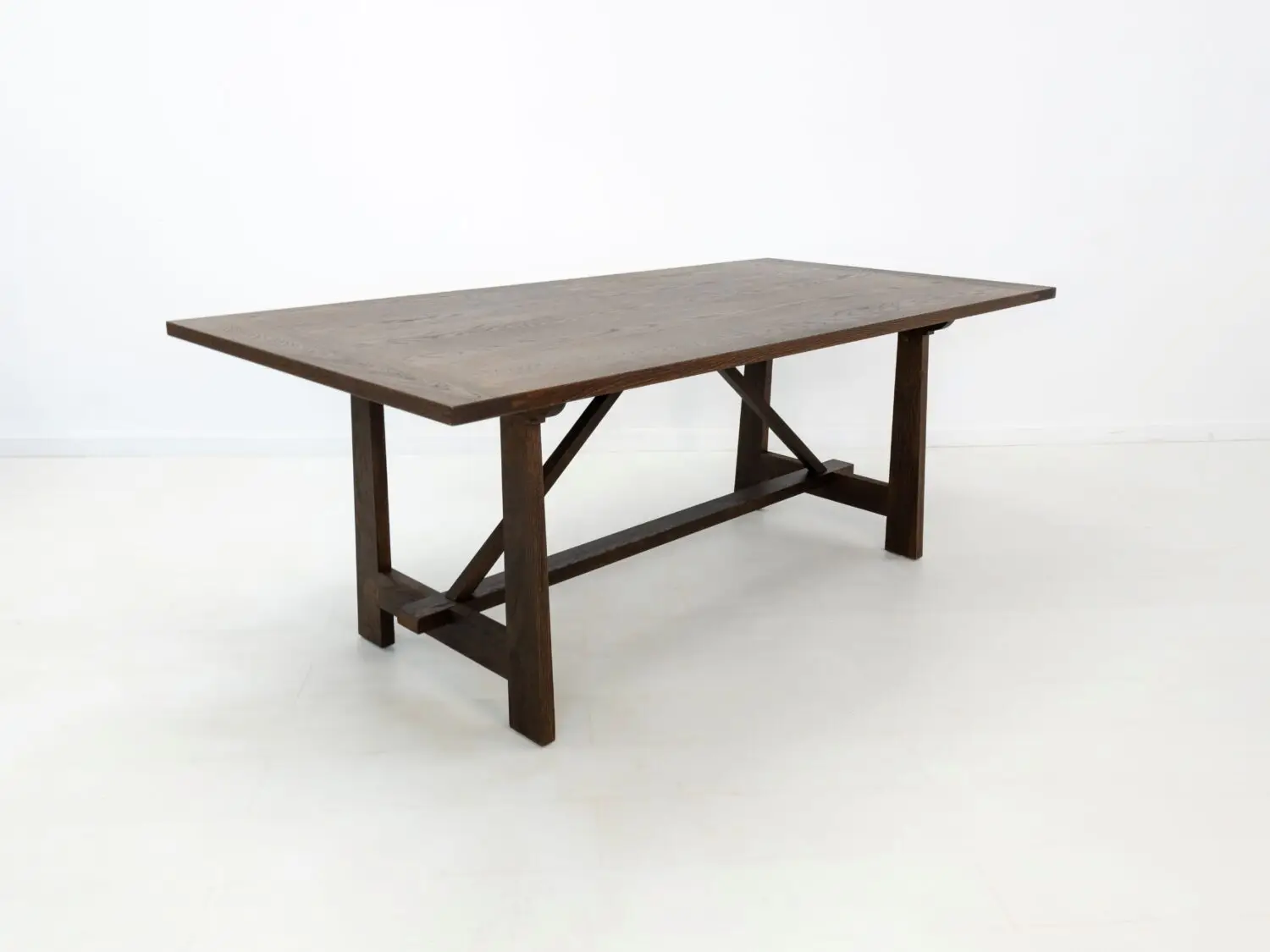 Angled view of the EDEN dining table  Custom white oak dining table in a rich stain featuring a seamless top and structural trestle base