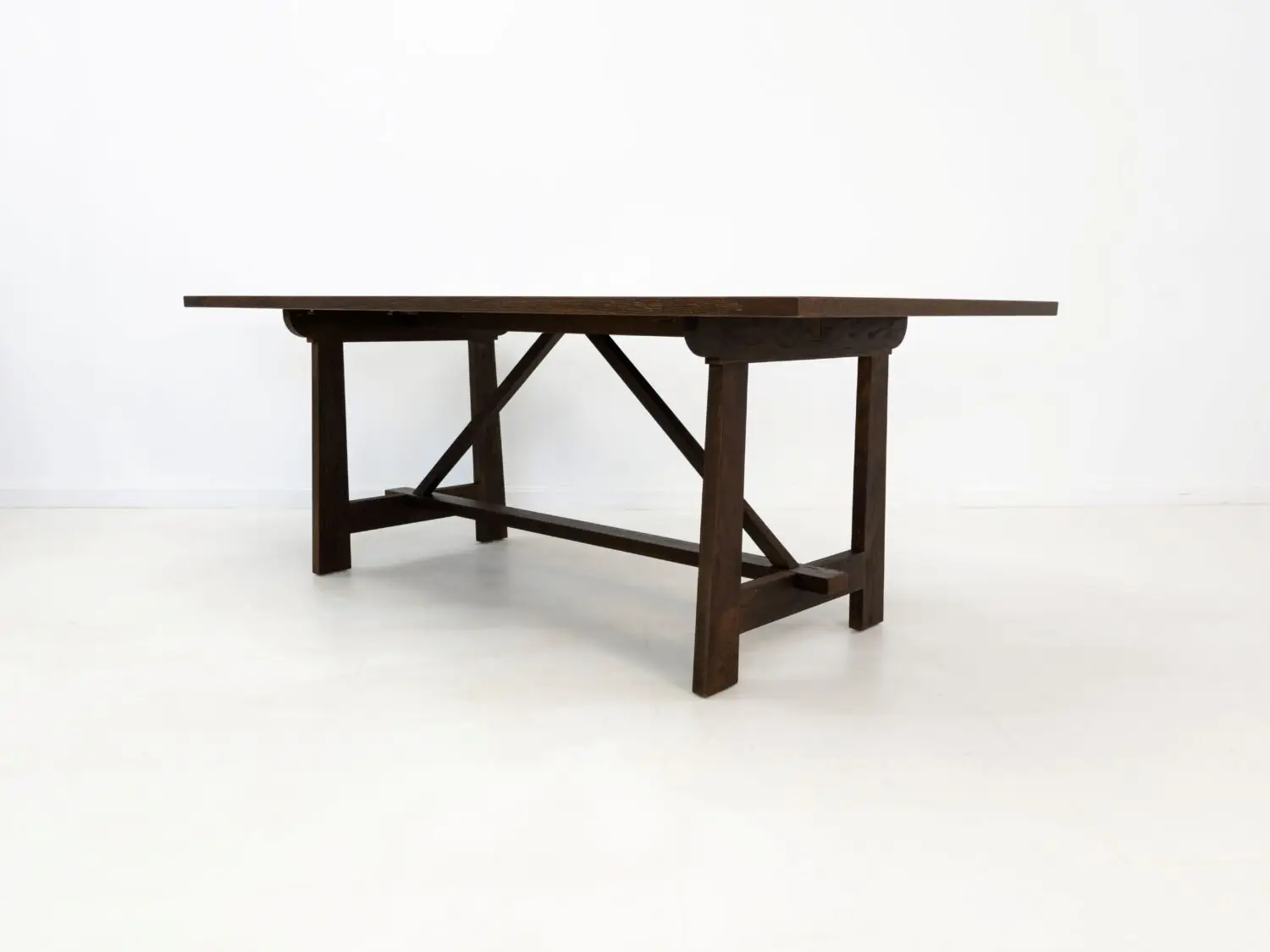 Angled view of the EDEN dining table  Custom white oak dining table in a rich stain featuring a seamless top and structural trestle base