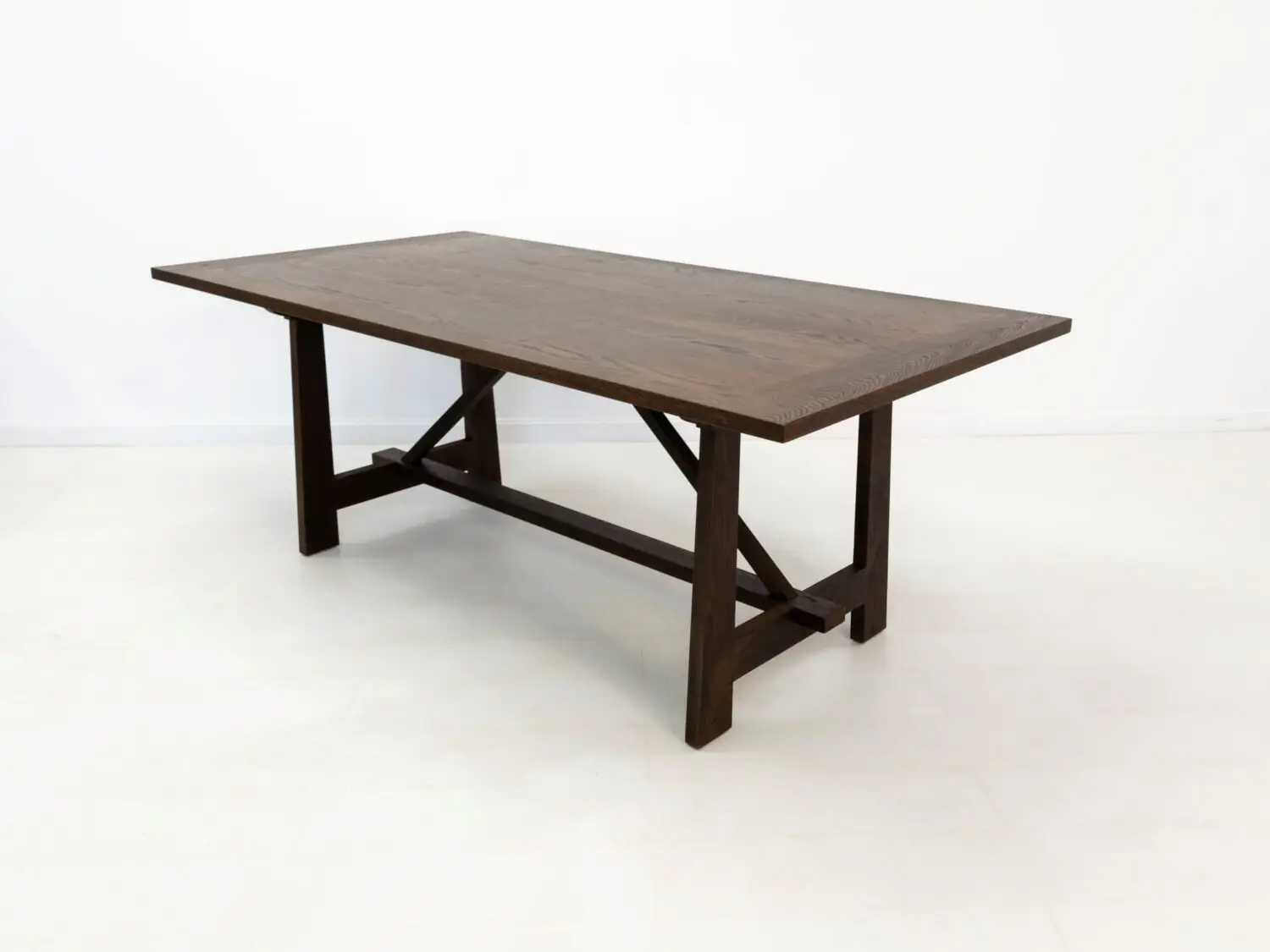 Angled view of the EDEN dining table  Custom white oak dining table in a rich stain featuring a seamless top and structural trestle base